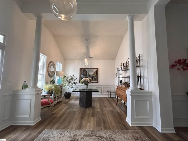 interior space featuring lofted ceiling, a decorative wall, a wainscoted wall, wood finished floors, and ornate columns