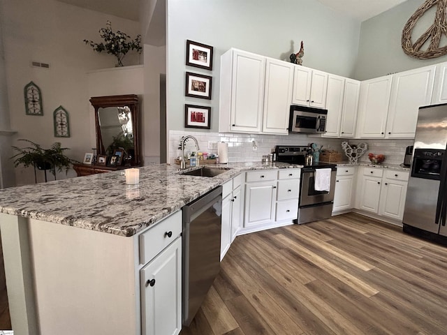 kitchen with a peninsula, appliances with stainless steel finishes, white cabinets, and a sink