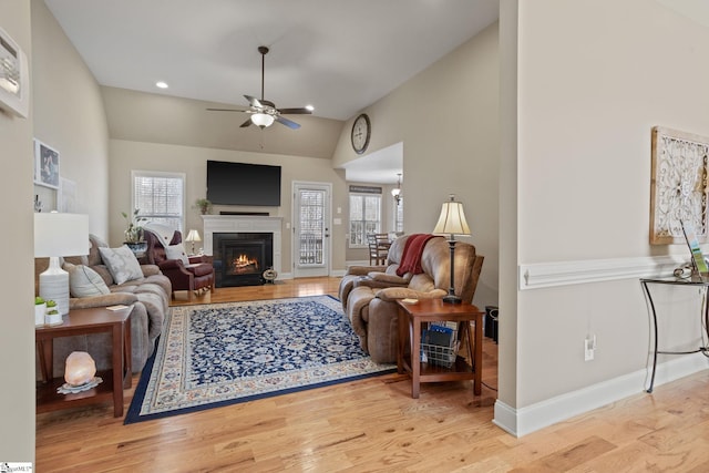 living room featuring baseboards, a ceiling fan, lofted ceiling, wood finished floors, and a lit fireplace