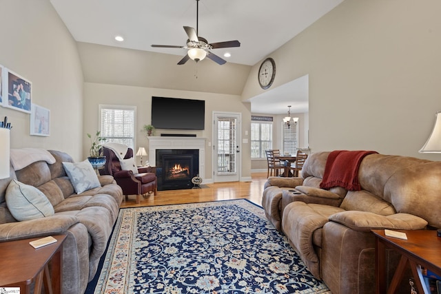 living room with lofted ceiling, recessed lighting, a fireplace with flush hearth, wood finished floors, and ceiling fan with notable chandelier