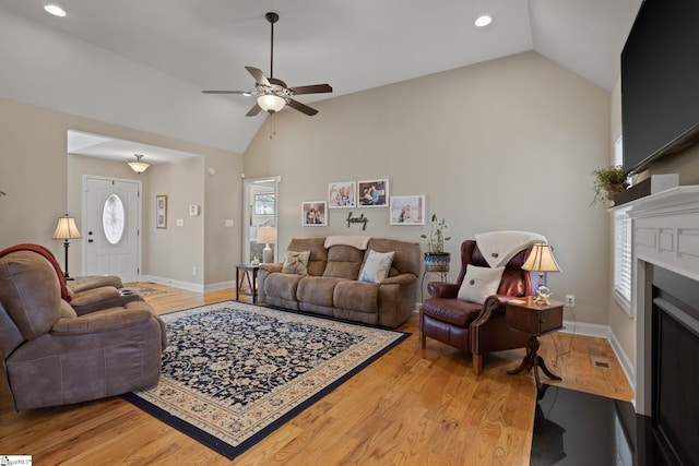 living area featuring lofted ceiling, light wood finished floors, and a fireplace with flush hearth