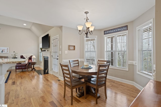 dining area with light wood-style flooring, a fireplace, baseboards, and a notable chandelier