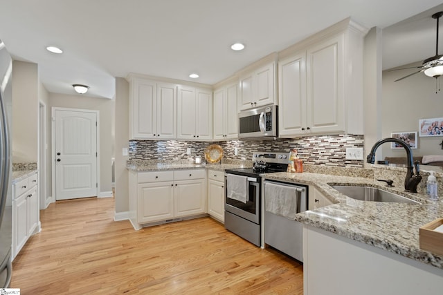 kitchen featuring stainless steel appliances, light wood finished floors, a sink, and decorative backsplash