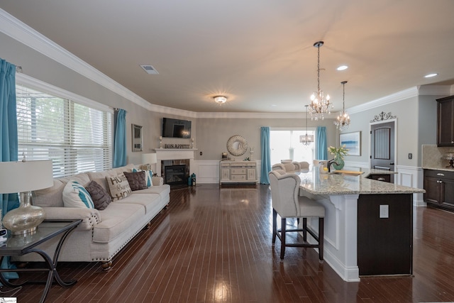 living area featuring a wealth of natural light, dark wood finished floors, visible vents, and crown molding