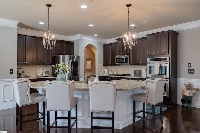 kitchen with a center island with sink, arched walkways, dark wood finished floors, stainless steel appliances, and dark brown cabinets