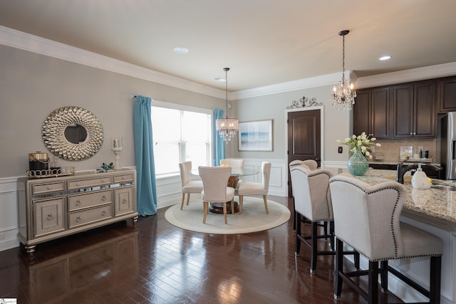 dining space with crown molding, a chandelier, dark wood-type flooring, and wainscoting