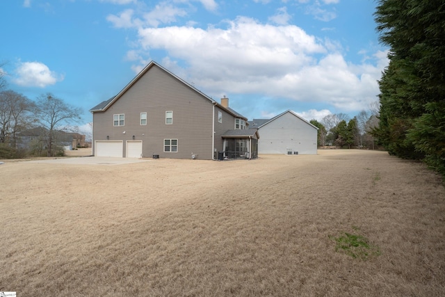 rear view of house featuring concrete driveway, a chimney, and an attached garage