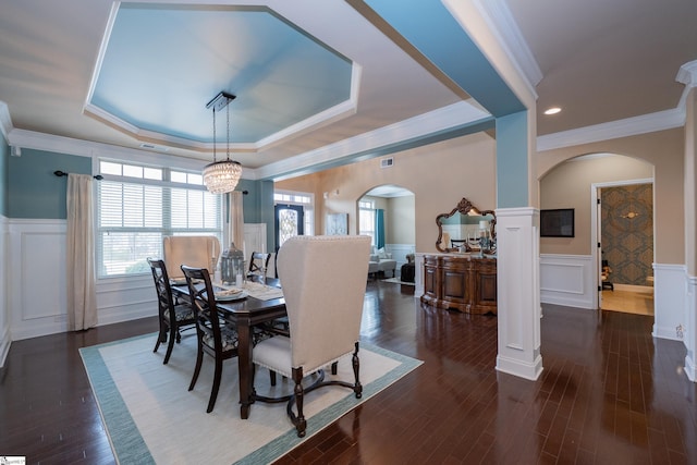 dining area featuring arched walkways, dark wood-style flooring, a wainscoted wall, and a decorative wall