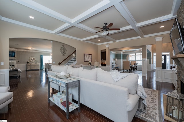 living room featuring arched walkways, a stone fireplace, coffered ceiling, and a decorative wall