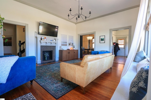 living area featuring ornamental molding, a tile fireplace, an inviting chandelier, and wood finished floors