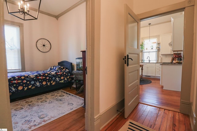 bedroom featuring hardwood / wood-style floors, an inviting chandelier, a sink, and crown molding