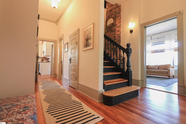 corridor featuring stairway, a high ceiling, ornamental molding, wood finished floors, and baseboards