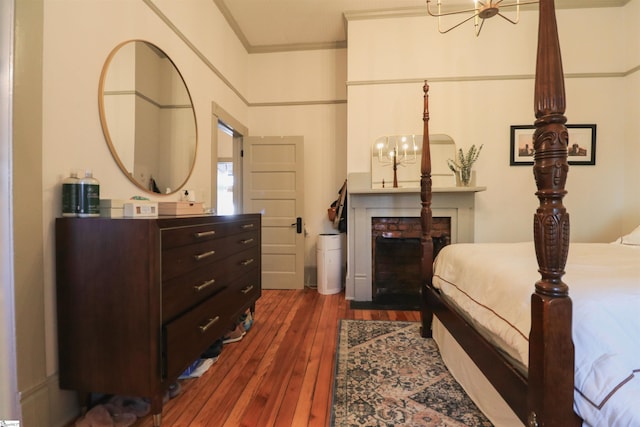 bedroom featuring dark wood-type flooring, a notable chandelier, ornamental molding, and a fireplace with flush hearth