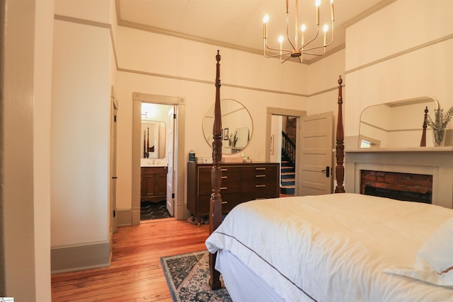 bedroom with a fireplace, baseboards, light wood-style floors, ensuite bath, and an inviting chandelier