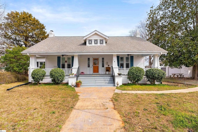 view of front facade featuring a front yard, covered porch, roof with shingles, and a chimney