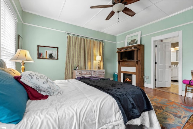 bedroom featuring ceiling fan, crown molding, a lit fireplace, and wood finished floors