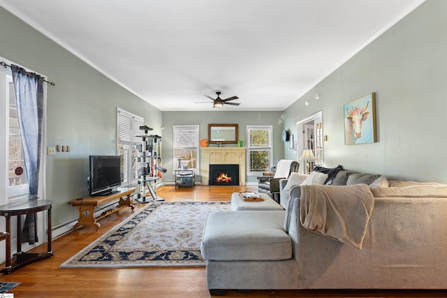 living area with ornamental molding, a brick fireplace, ceiling fan, and wood finished floors