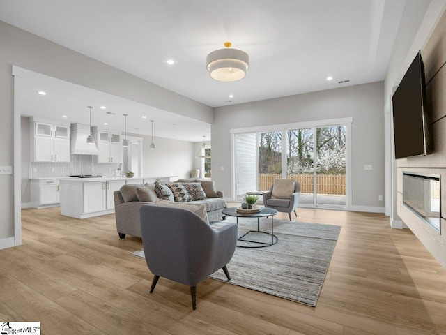 living area featuring visible vents, baseboards, a glass covered fireplace, light wood-style floors, and recessed lighting