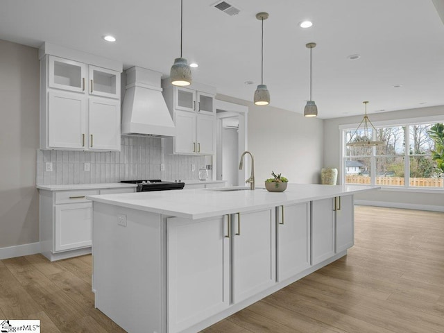 kitchen with custom range hood, visible vents, backsplash, white cabinets, and a sink