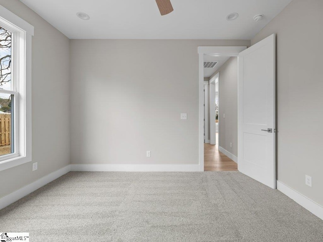 carpeted empty room featuring a ceiling fan, visible vents, and baseboards