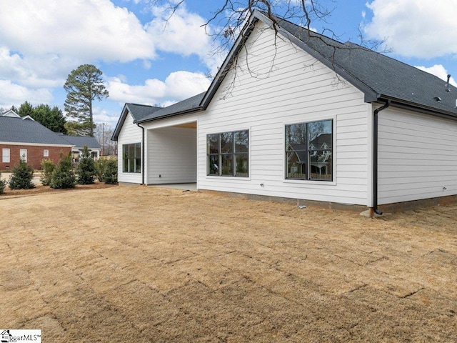 rear view of property featuring roof with shingles and a lawn