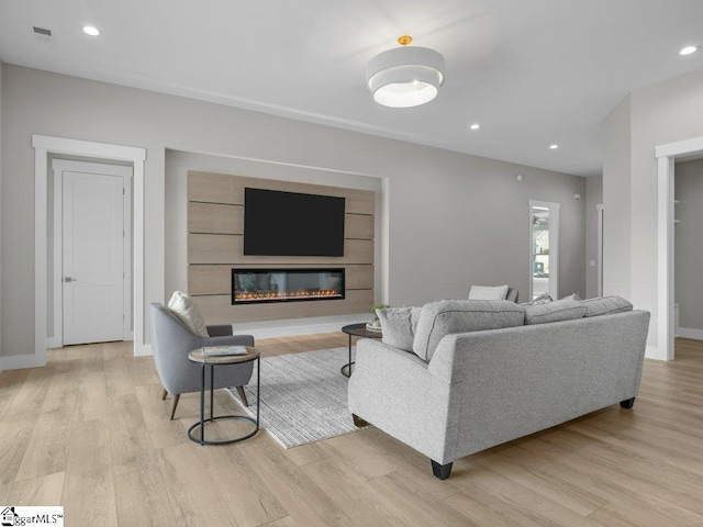 living room featuring a glass covered fireplace, visible vents, recessed lighting, and wood finished floors