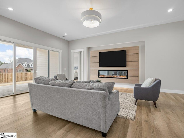 living room with light wood finished floors, recessed lighting, baseboards, and a glass covered fireplace