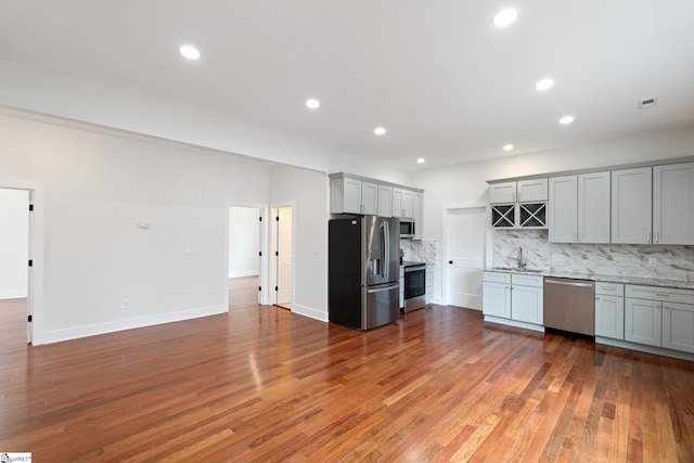 kitchen with wood-type flooring, appliances with stainless steel finishes, a sink, gray cabinets, and backsplash