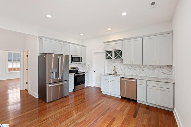 kitchen featuring stainless steel appliances, a sink, visible vents, tasteful backsplash, and wood-type flooring