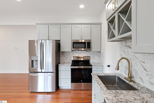 kitchen with light stone counters, stainless steel appliances, tasteful backsplash, light wood-style floors, and a sink