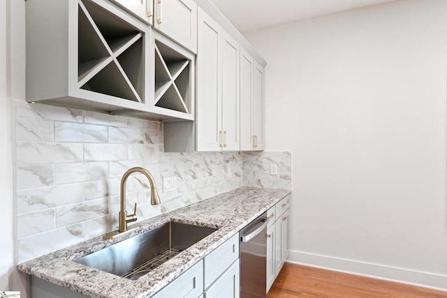 kitchen with light stone counters, a sink, baseboards, decorative backsplash, and dishwasher