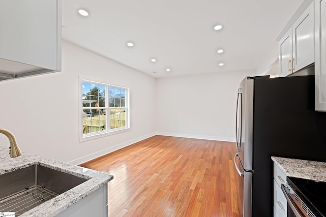 kitchen featuring light stone counters, freestanding refrigerator, light wood-style floors, a sink, and recessed lighting