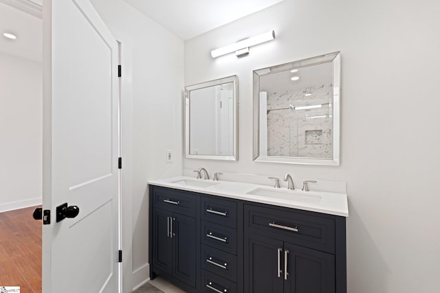 bathroom with double vanity, a walk in shower, a sink, and wood finished floors