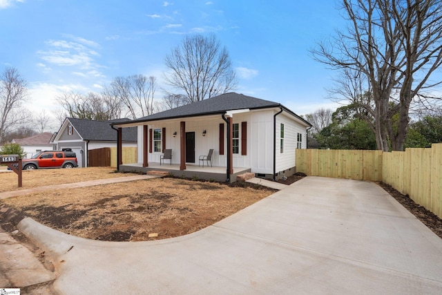 view of front of house with a shingled roof, covered porch, and fence