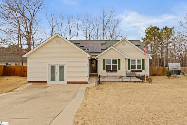 rear view of property featuring french doors, roof with shingles, fence, and roof mounted solar panels