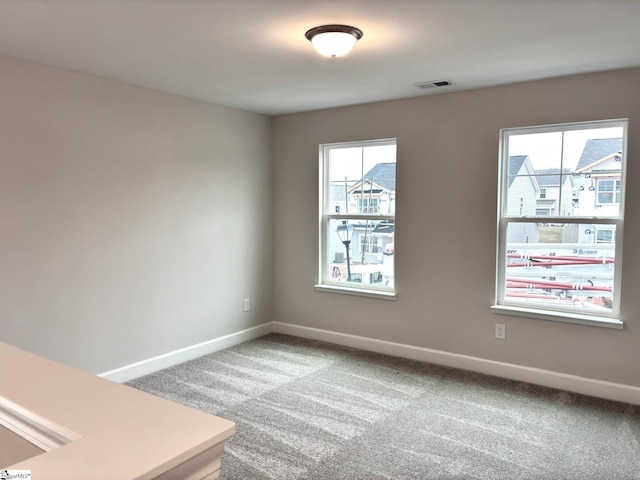 empty room featuring a wealth of natural light, carpet floors, visible vents, and baseboards