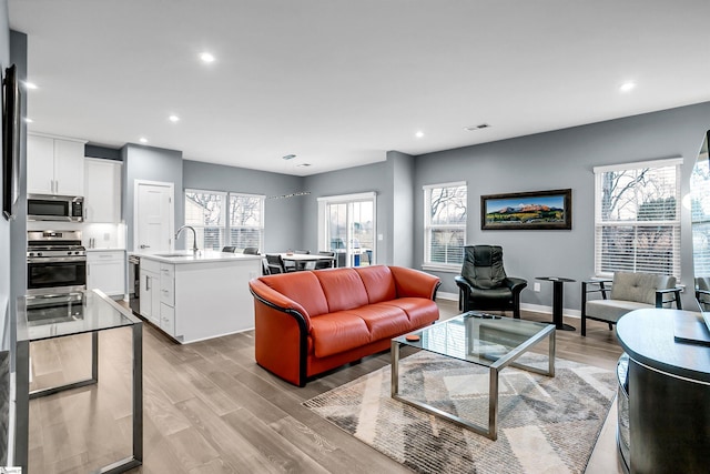 living area with light wood-style flooring, visible vents, baseboards, and recessed lighting