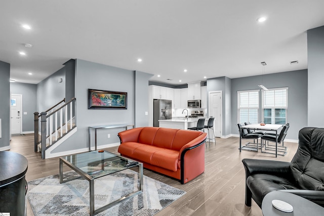 living area featuring light wood-type flooring, stairway, baseboards, and recessed lighting