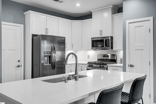 kitchen featuring stainless steel appliances, a sink, white cabinetry, backsplash, and a kitchen bar