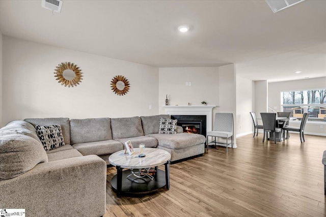 living room featuring baseboards, visible vents, wood finished floors, and a high end fireplace