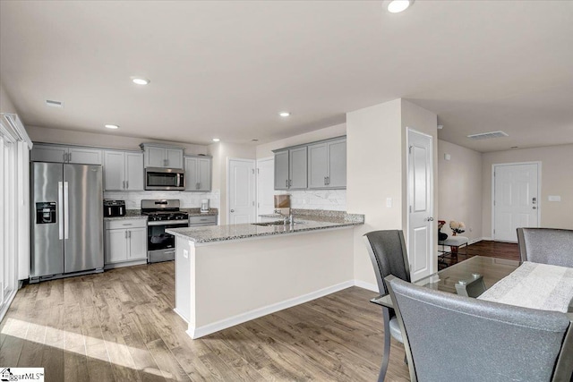 kitchen featuring gray cabinetry, visible vents, appliances with stainless steel finishes, light stone countertops, and light wood finished floors