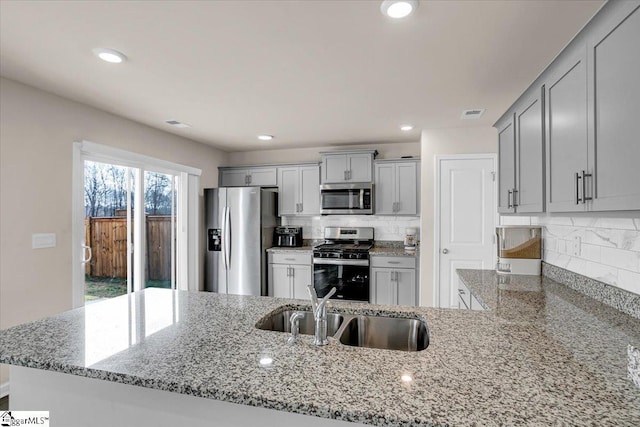 kitchen featuring gray cabinetry, stainless steel appliances, a sink, backsplash, and light stone countertops