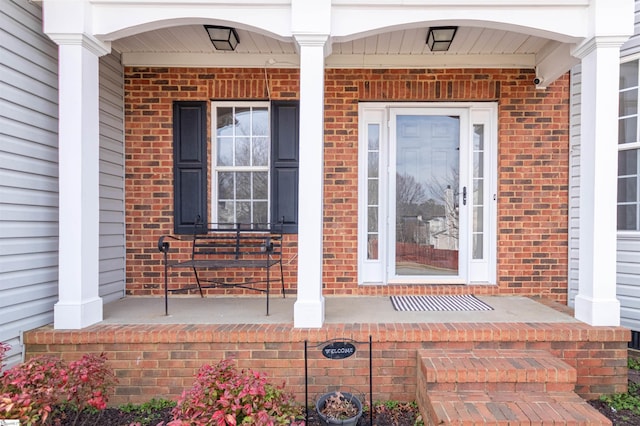 view of exterior entry with brick siding and covered porch