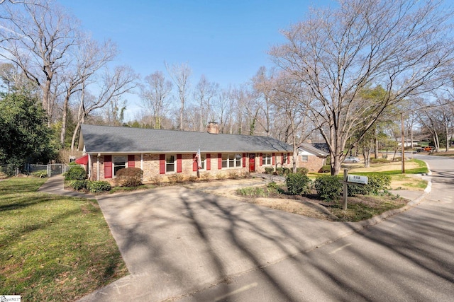 ranch-style home featuring driveway, brick siding, a chimney, fence, and a front yard