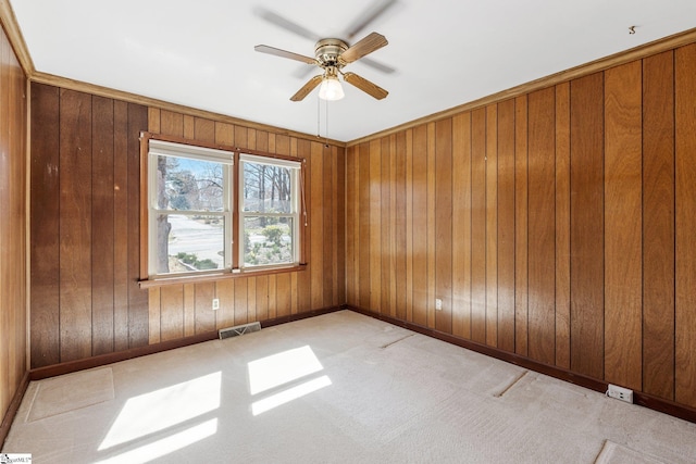 carpeted spare room featuring ceiling fan, wood walls, visible vents, and baseboards