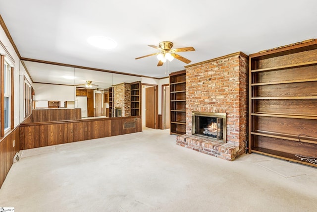 unfurnished living room with ceiling fan, carpet floors, a fireplace, built in features, and crown molding