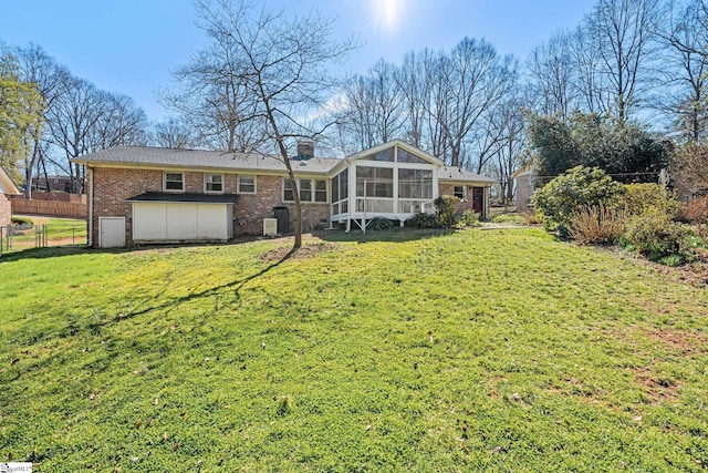 back of house with a lawn, a sunroom, a chimney, fence, and brick siding