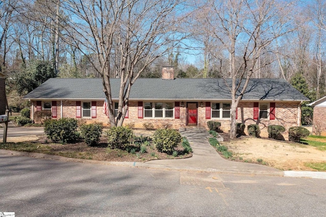 ranch-style home featuring a shingled roof, a chimney, and brick siding