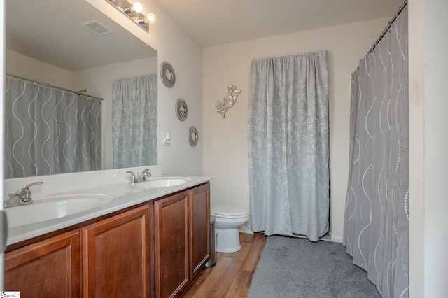 full bathroom with double vanity, visible vents, a sink, and wood finished floors