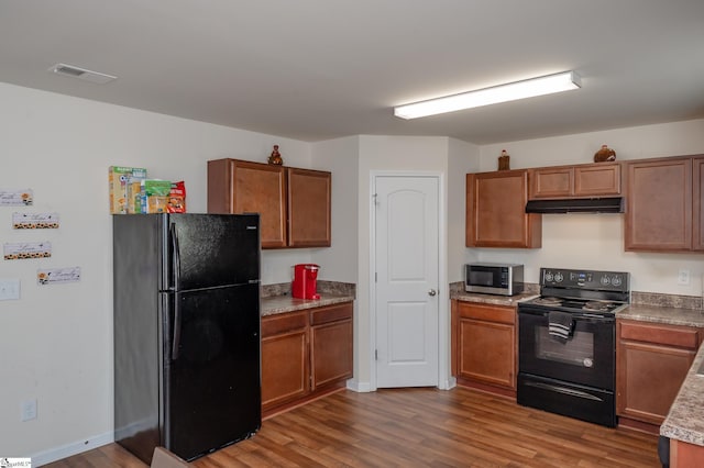 kitchen featuring brown cabinets, dark wood finished floors, visible vents, under cabinet range hood, and black appliances